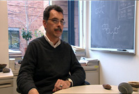 Dr. Julian Simon sitting at his desk talking to the camera
